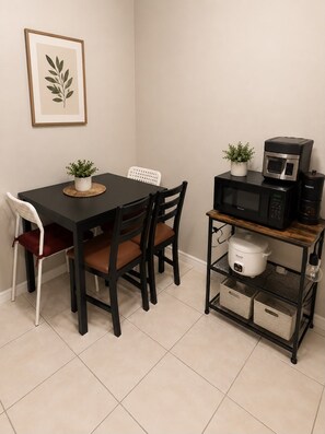 A dining area with a black table, two chairs, a framed plant, a microwave, and a rice cooker on a shelf. - Enjoyable 2-bedroom apartment at St. Peters; Near STL (St. Peters)