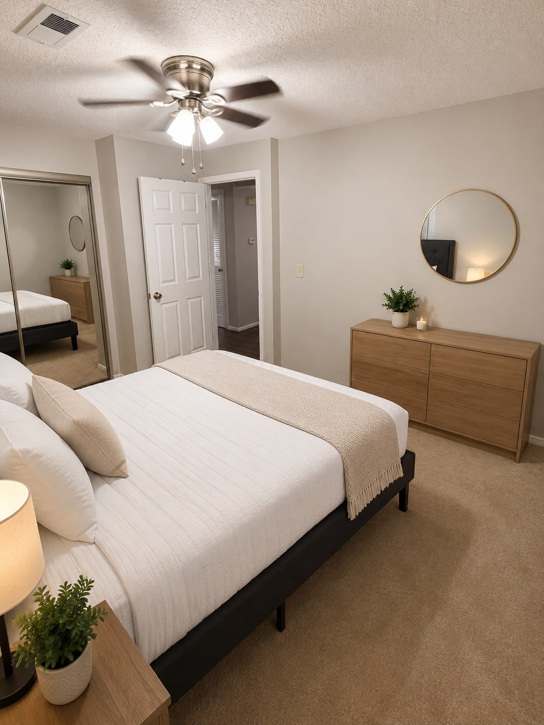 A bedroom with a bed, a dresser, a mirror, a ceiling fan, and a door leading to another room.