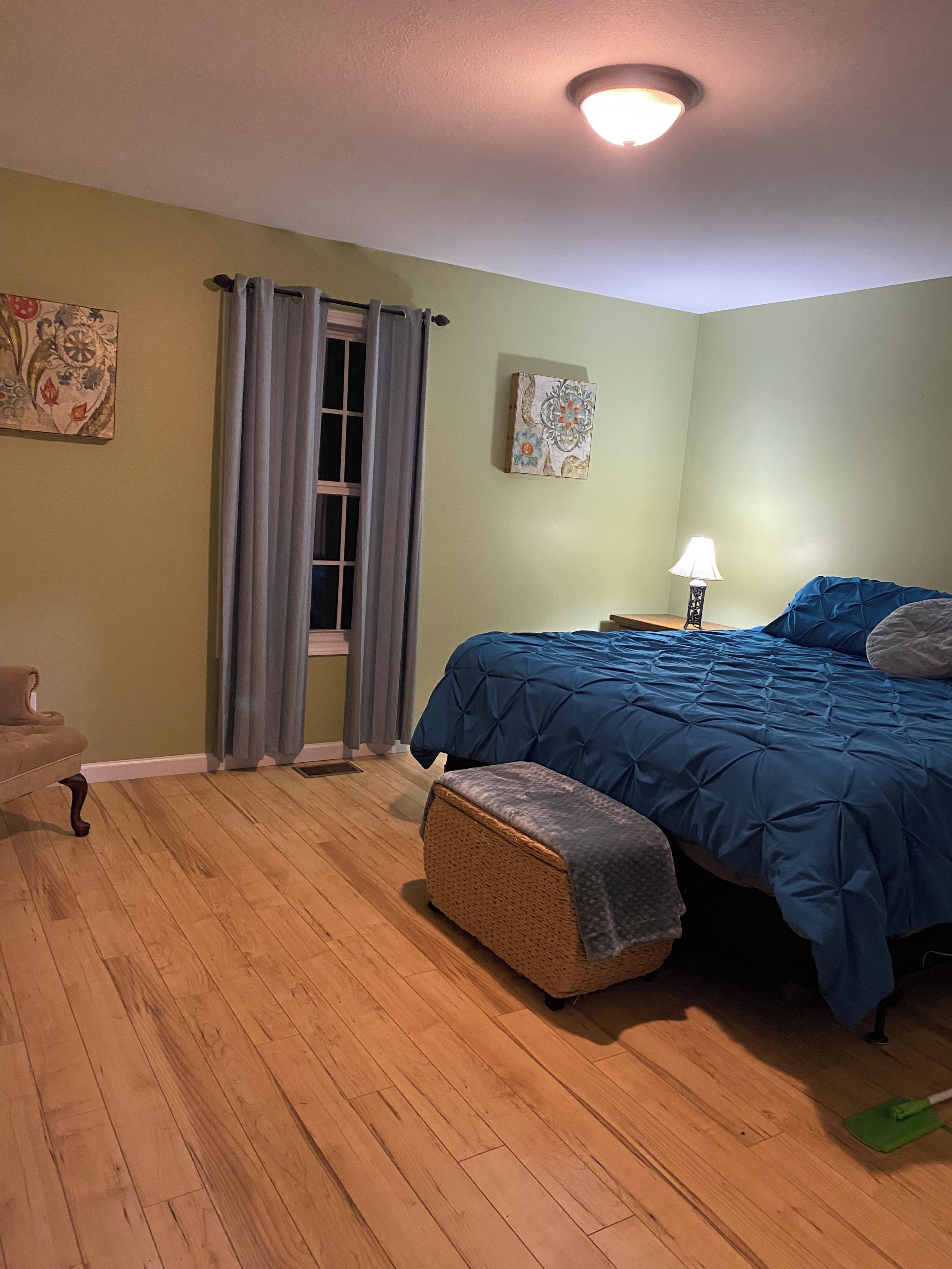Une chambre à coucher avec un lit, une chaise, une lampe et une fenêtre avec des rideaux.