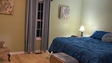 Une chambre à coucher avec un lit, une chaise, une lampe et une fenêtre avec des rideaux.