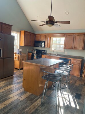 A kitchen with wooden cabinets, a stainless steel refrigerator, a microwave, a stove, and a ceiling fan. - Lake Living at it’s Best (Dover)