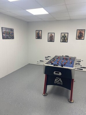 A foosball table in a room with white walls and a grey floor, with four framed pictures on the wall. - Lake Living at it’s Best (Dover)