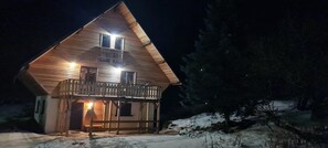 A wooden cabin with a balcony, a snow-covered ground, and a dark surrounding environment. - Large 4-Star Chalet at Balné ô Sancy (Chastreix)