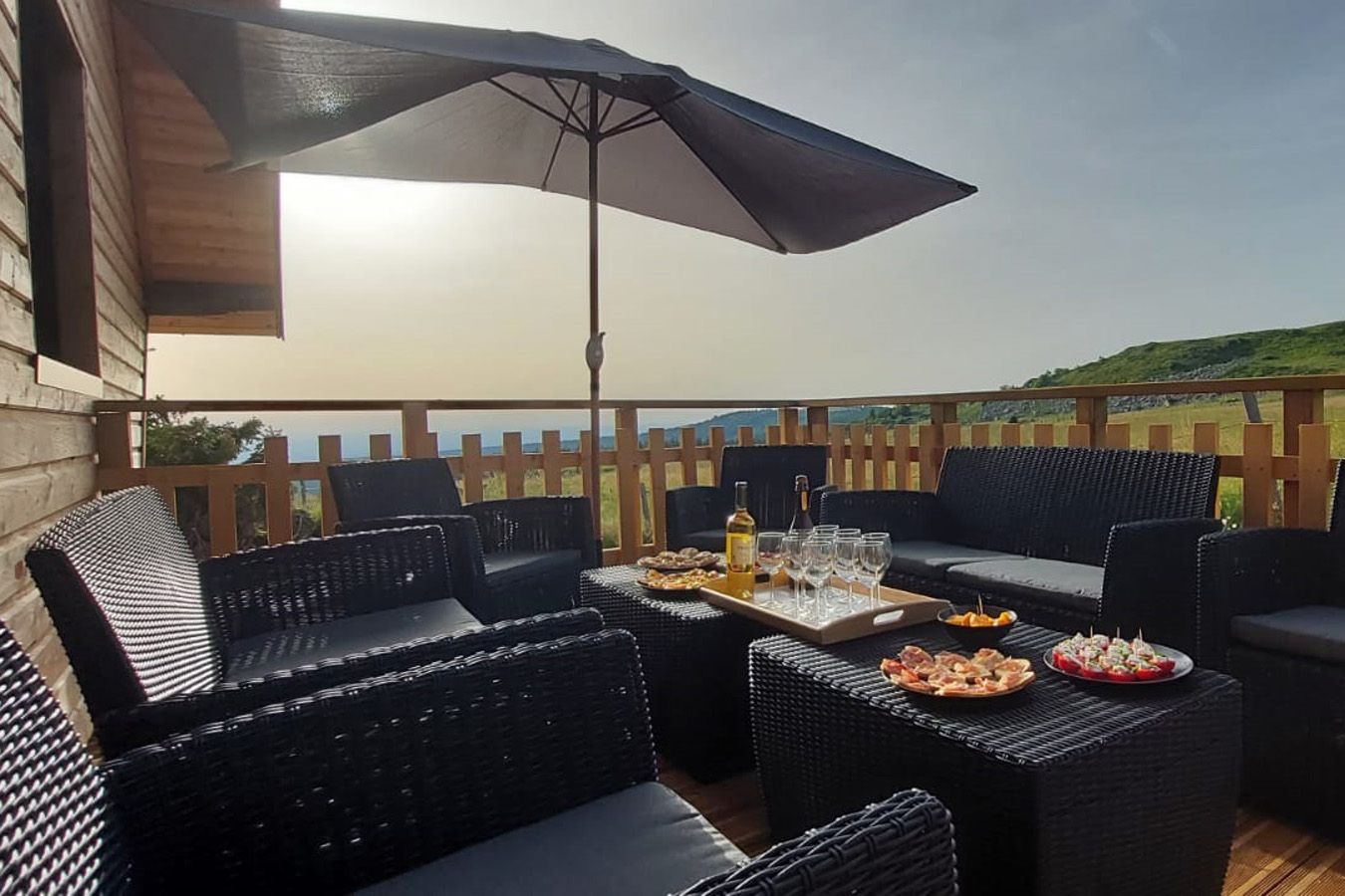 An outdoor patio with wicker furniture, a table set with food and drinks, and a view of the landscape.