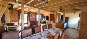 Ein Holzinnenraum mit Essbereich, einer Couch und einer durchgehenden Tür erkennbaren Küche.