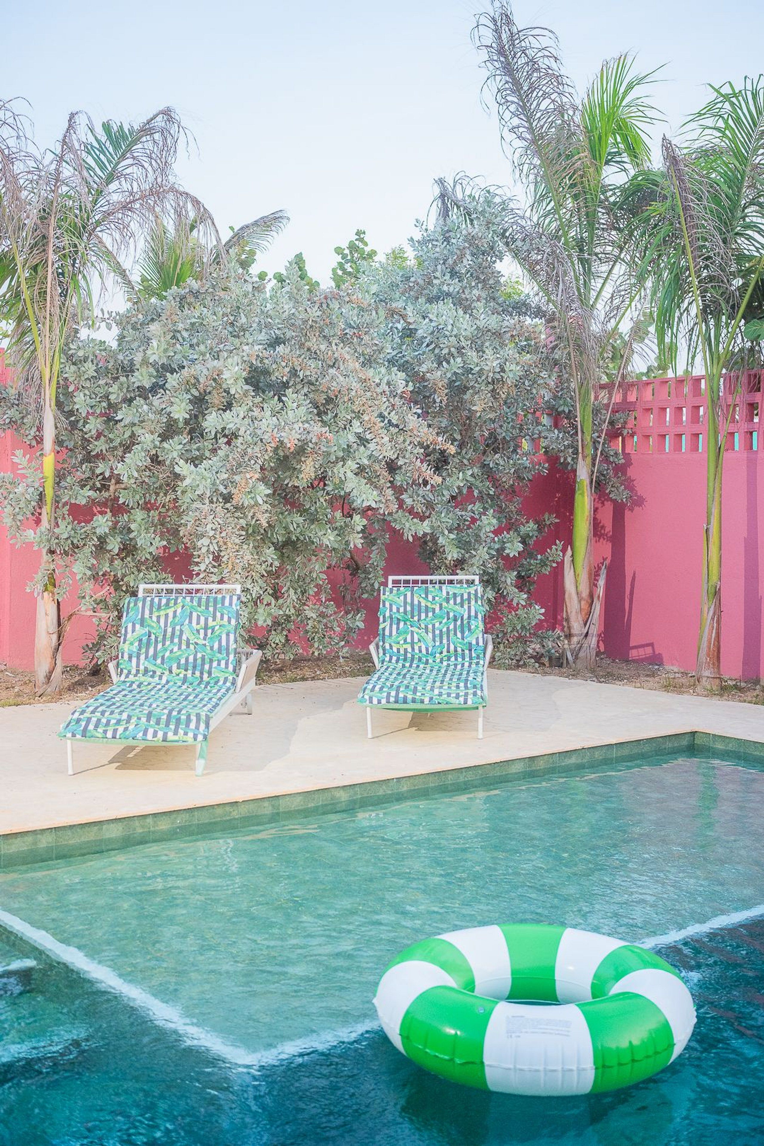 A swimming pool with two lounge chairs and a green inflatable ring.