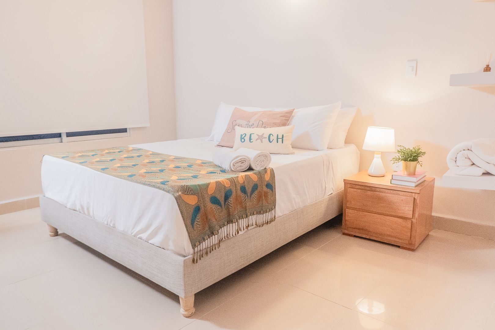 A neatly made bed with a patterned throw, a bedside table with a lamp, and a wall-mounted phone.
