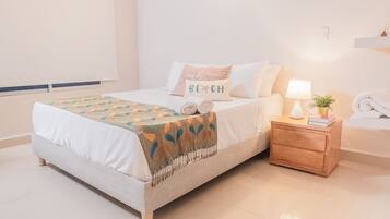 A neatly made bed with a patterned throw, a bedside table with a lamp, and a wall-mounted phone.