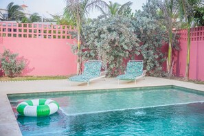 Une piscine avec deux chaises longues et un flotteur gonflable vert et blanc.