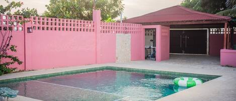 A swimming pool with a pink fence, a covered area, and a green inflatable float.