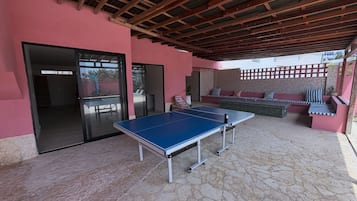 An outdoor area with a ping pong table, a seating area with cushions, and a covered space with a wooden ceiling.