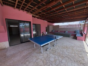 Un espace extérieur comprenant une table de ping-pong, un coin salon avec des coussins et un espace abrité doté d’un plafond en bois.