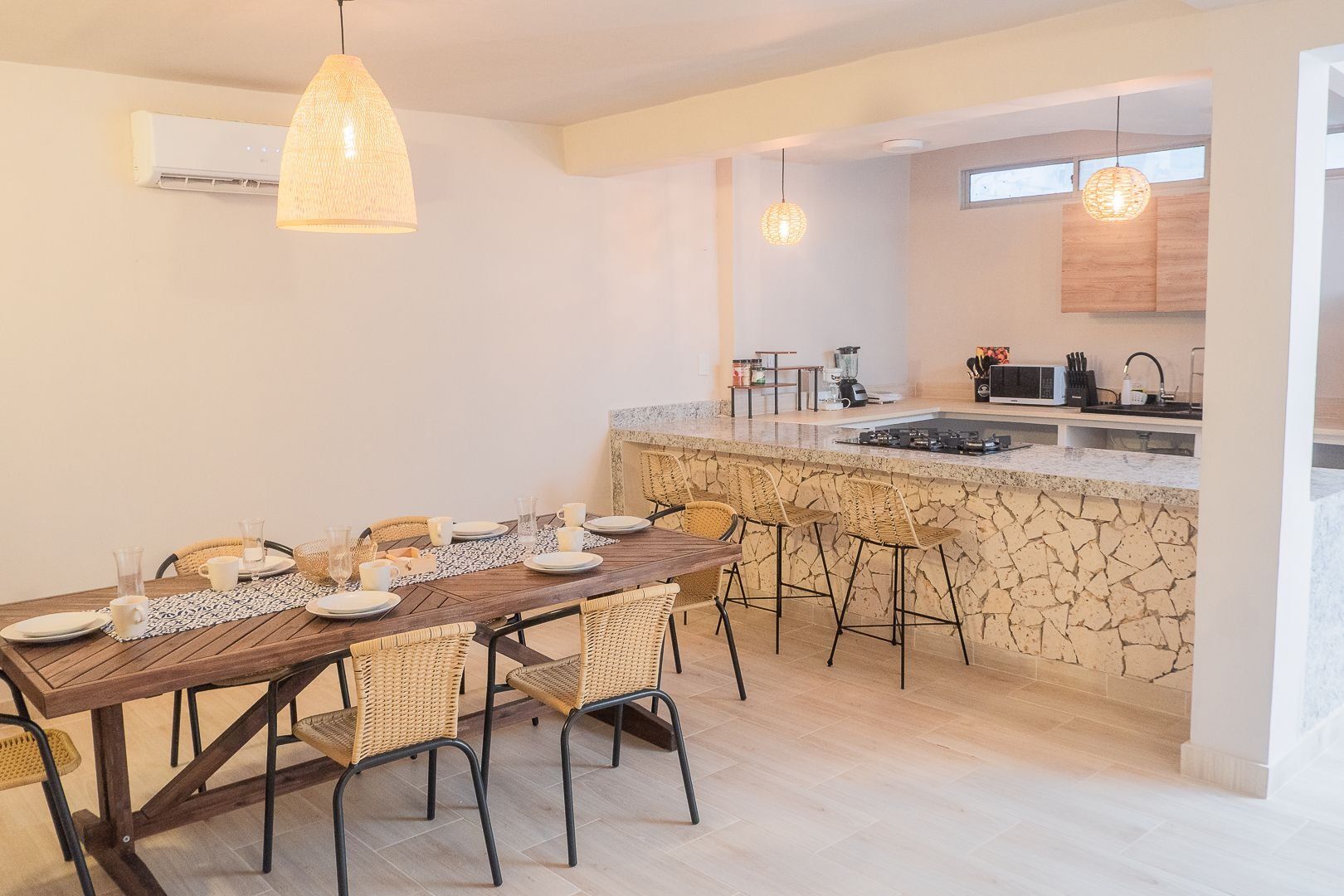 A dining area with a wooden table and wicker chairs, a kitchen with a stone island, and pendant lighting.