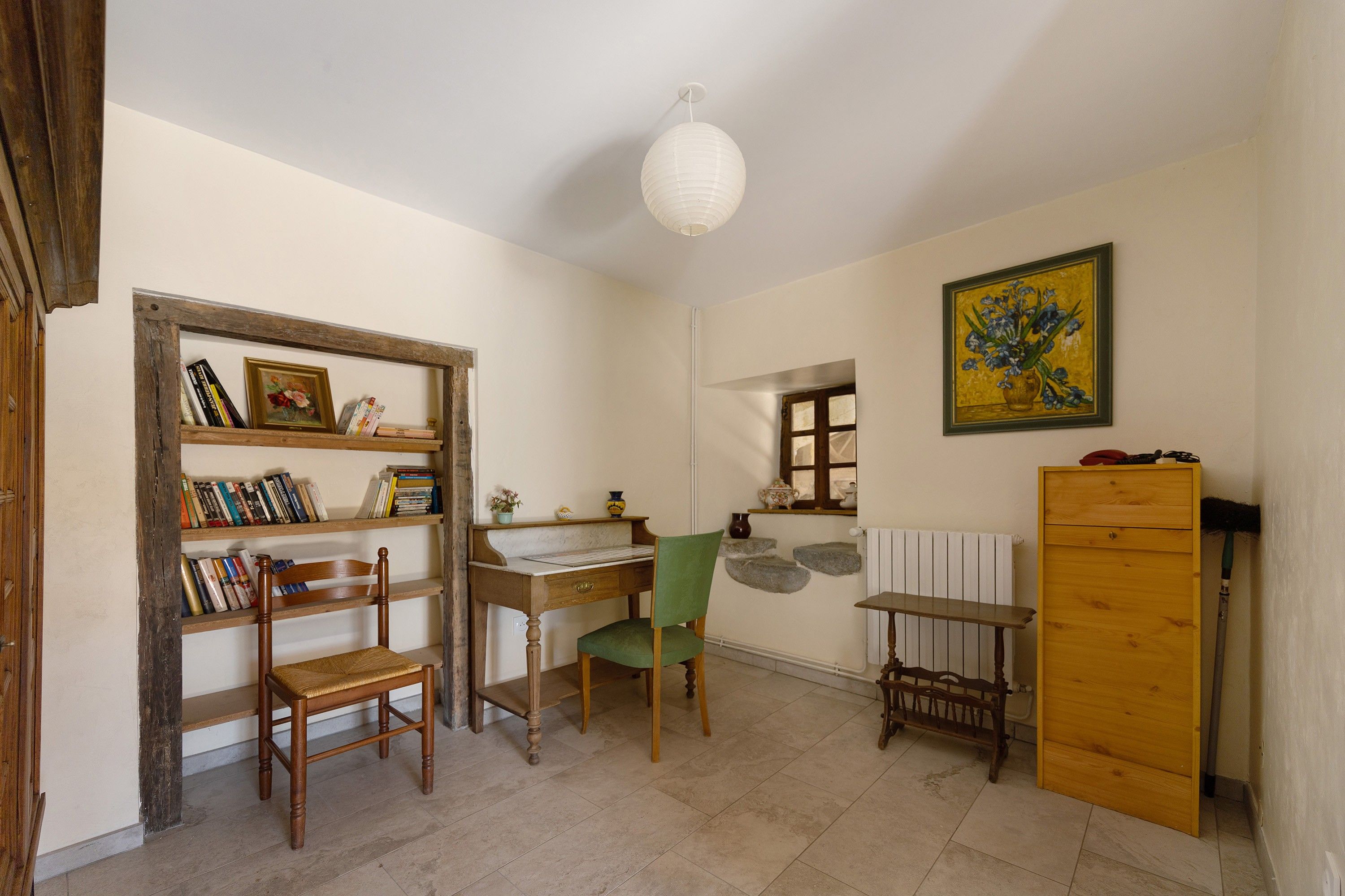 Una stanza con una scrivania in legno, una sedia, una libreria, un termosifone e un quadro appeso al muro.