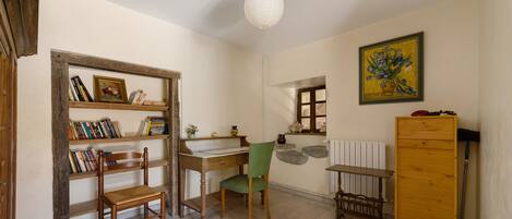 Una stanza con una scrivania in legno, una sedia, una libreria, un termosifone e un quadro appeso al muro.