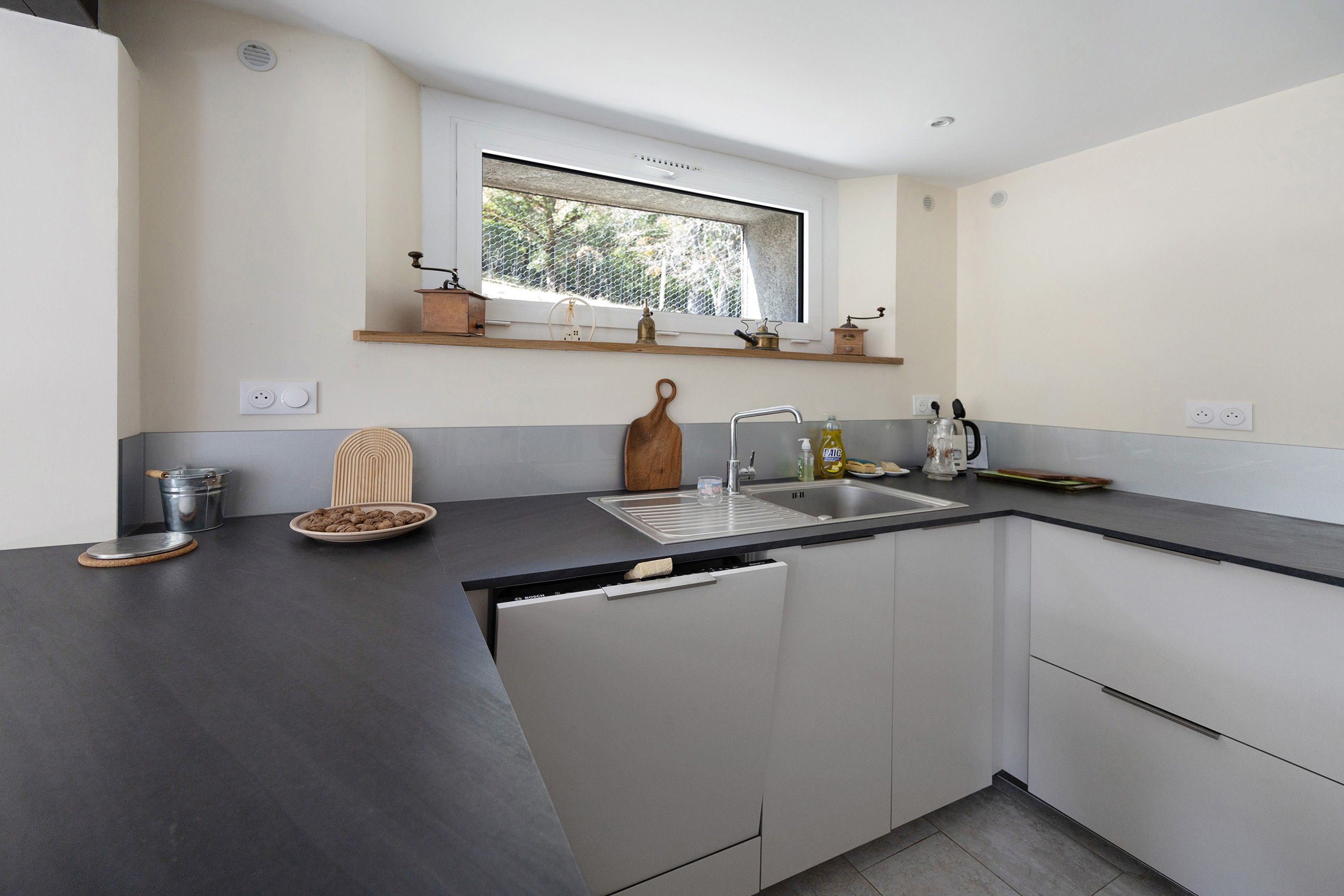 A modern kitchen with a built-in dishwasher, a sink, and a window above the countertop.