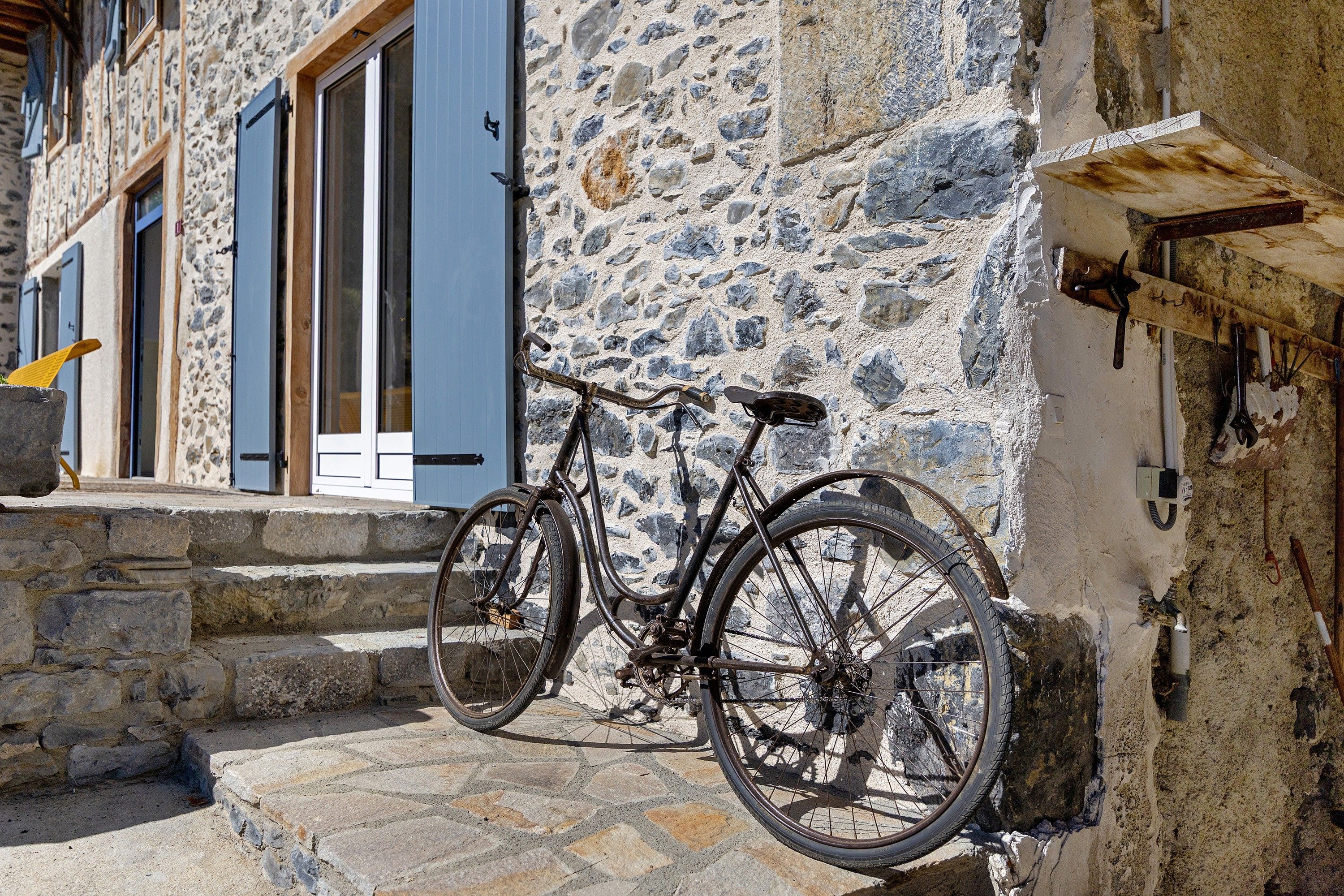 A bicycle parked against a stone wall with a wooden beam and a metal rack.