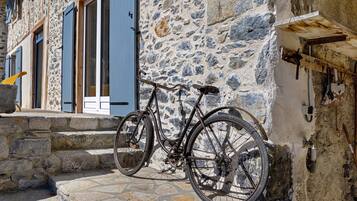 A bicycle parked against a stone wall with a wooden beam and a metal rack.