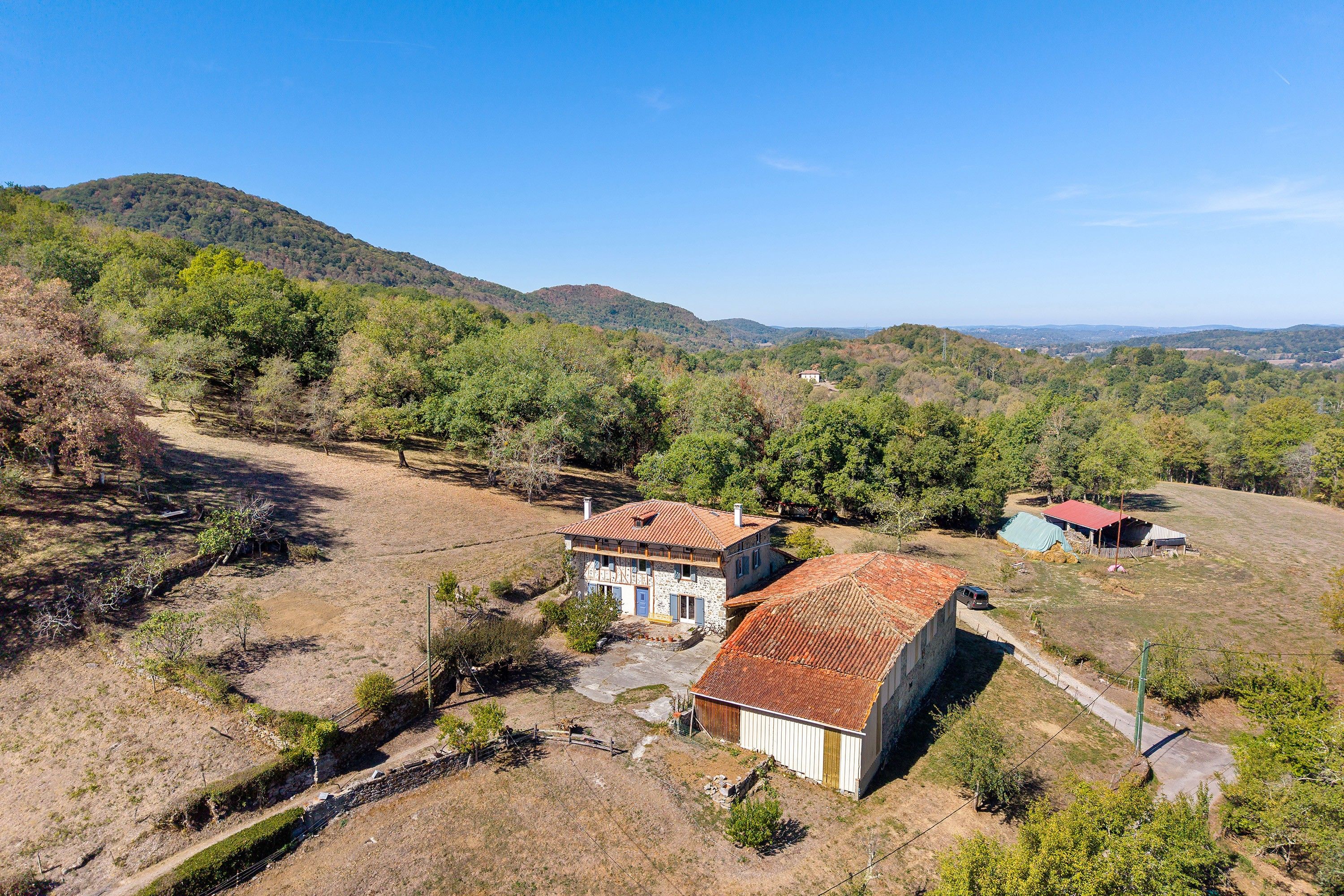 Propiedad rural con casa de piedra, granero de techo rojo y un área cercada con árboles.