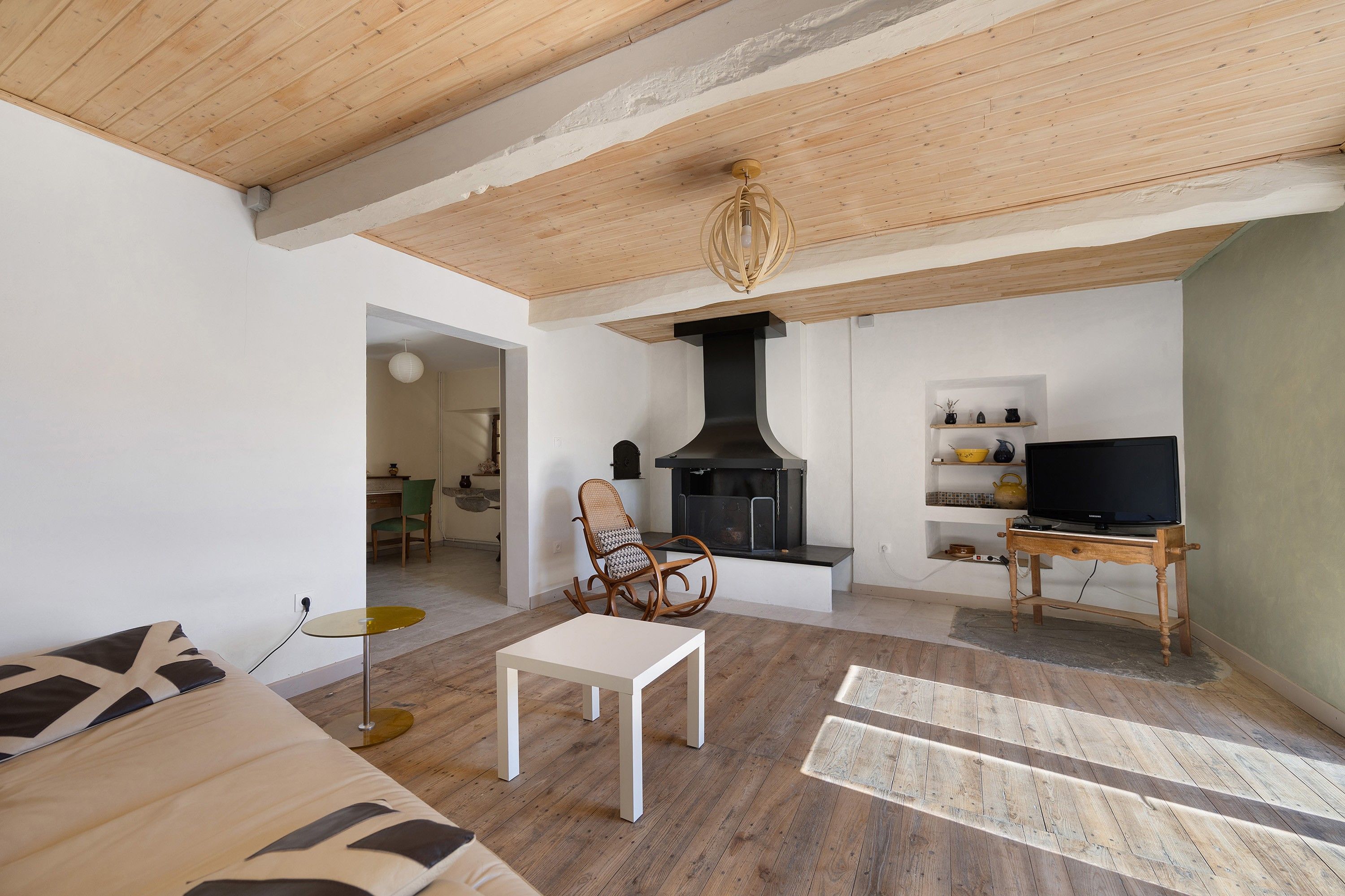 A living room with a sofa, a table, a television on a stand, a fireplace, and a ceiling light fixture.