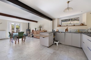 A modern kitchen with a central island, built-in appliances, and a dining area with a view. - Country House “Chez Julia” with Shared Terrace, Private Garden, and Wi-Fi (Cazavet)