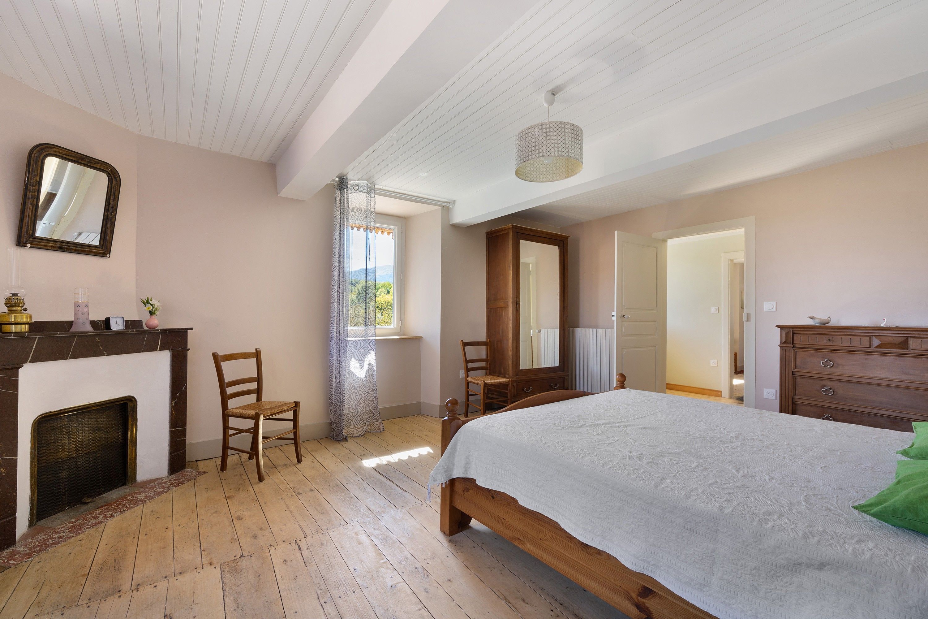 Un dormitorio con una cama de madera, un aparador, una silla, una chimenea y una ventana con cortinas.