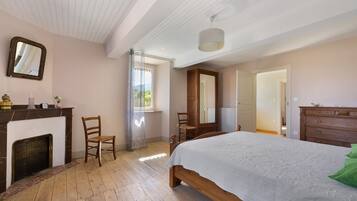 Un dormitorio con una cama de madera, un aparador, una silla, una chimenea y una ventana con cortinas.