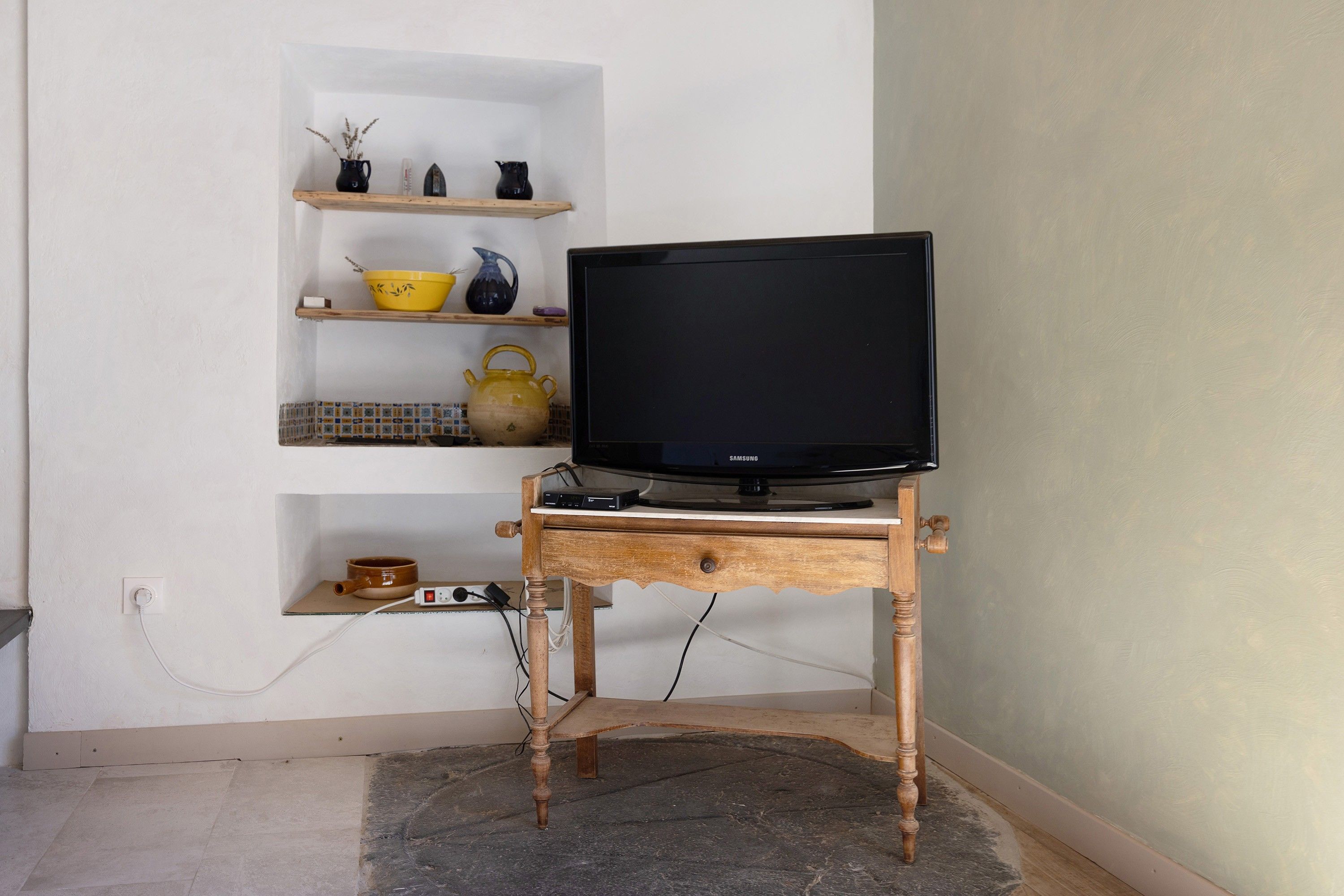 A television on a wooden stand with a shelf above it containing various items.