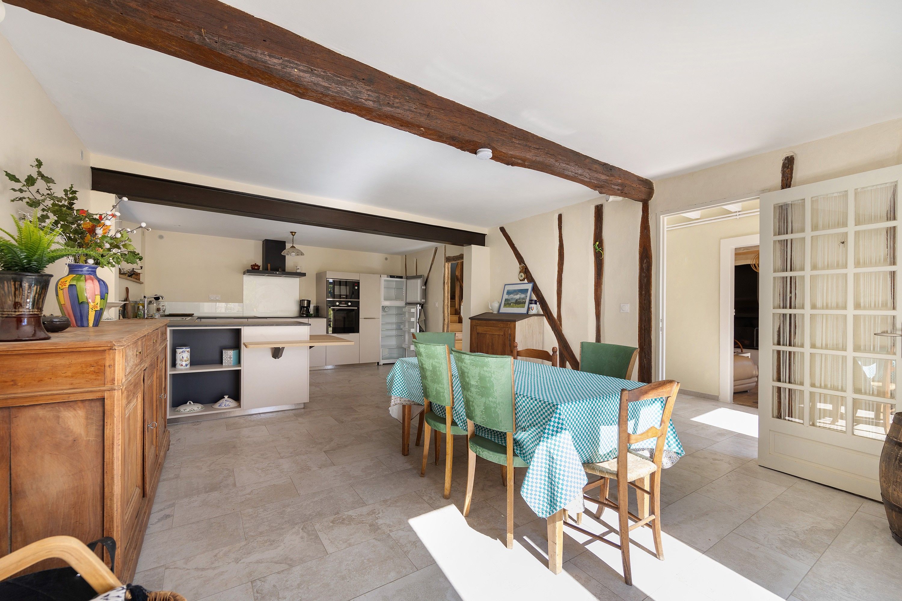 Una cocina amplia con electrodomésticos modernos, un comedor con mantel a cuadros y un techo rústico de madera.