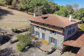 A two-story stone house with a tiled roof, a balcony, and a small garden area with potted plants. - Country House “Chez Julia” with Shared Terrace, Private Garden, and Wi-Fi (Cazavet)