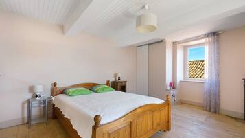 Een slaapkamer met een houten bed, een nachtkastje, een lamp, een raam met gordijnen en een plafondlamp.