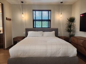 A bedroom with a large bed, two bedside tables, a window with blinds, and a potted plant. - Boutique Canopy Studio at Jackson Market (Culver City)