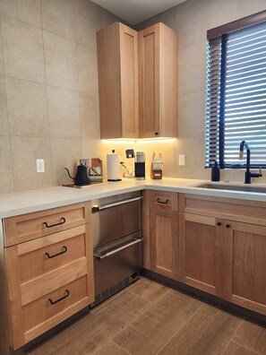 A modern kitchen with wooden cabinets, a stainless steel range, and a window with blinds. - Boutique Canopy Studio at Jackson Market (Culver City)