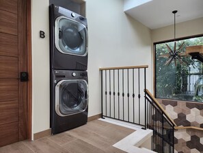 A laundry room with stacked washers and dryers, a wooden door, and a staircase with a geometric tile wall. - Boutique Canopy Studio at Jackson Market (Culver City)