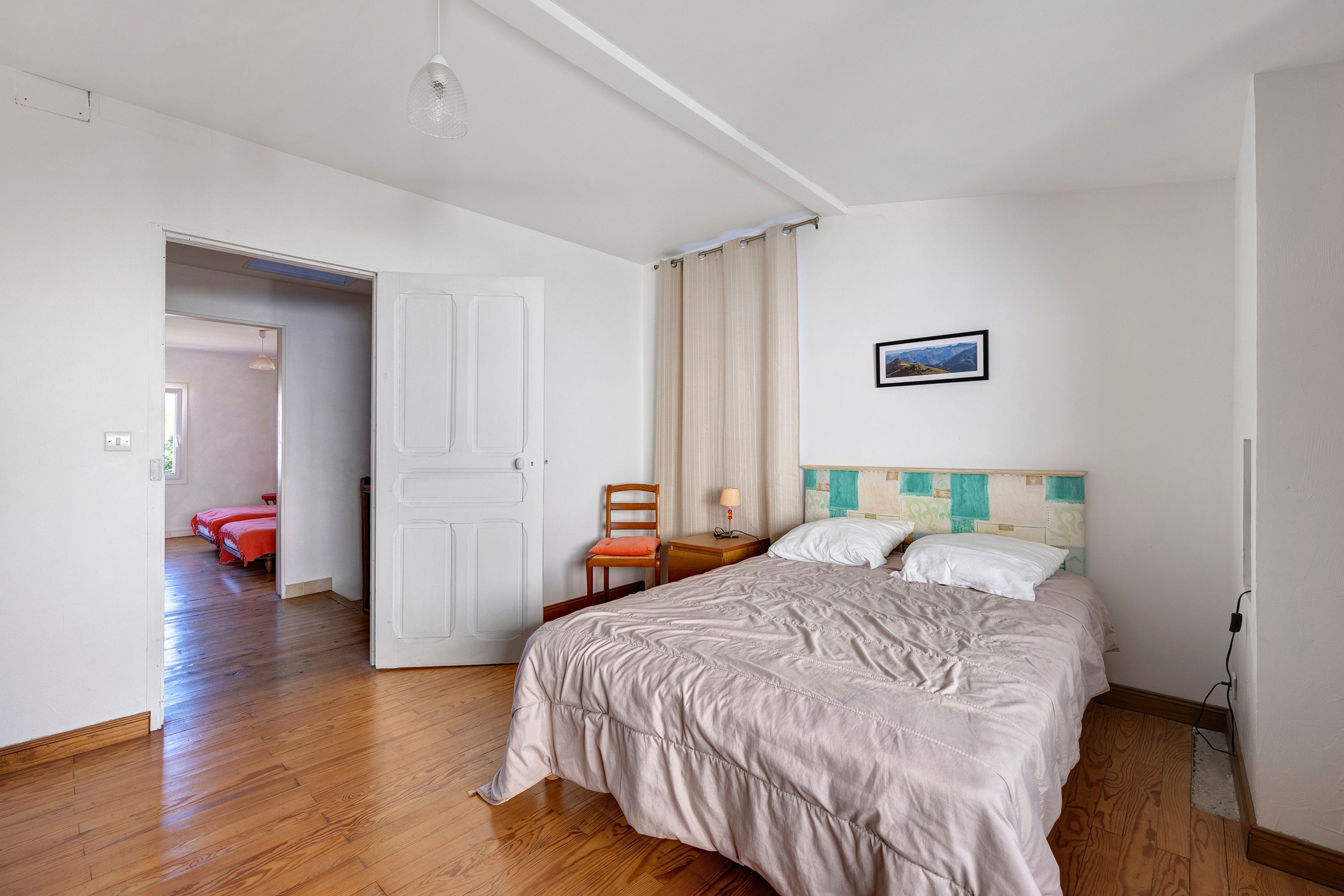 Habitación de hotel con una cama, una silla, una mesita de noche, una lámpara y un cuadro en la pared.