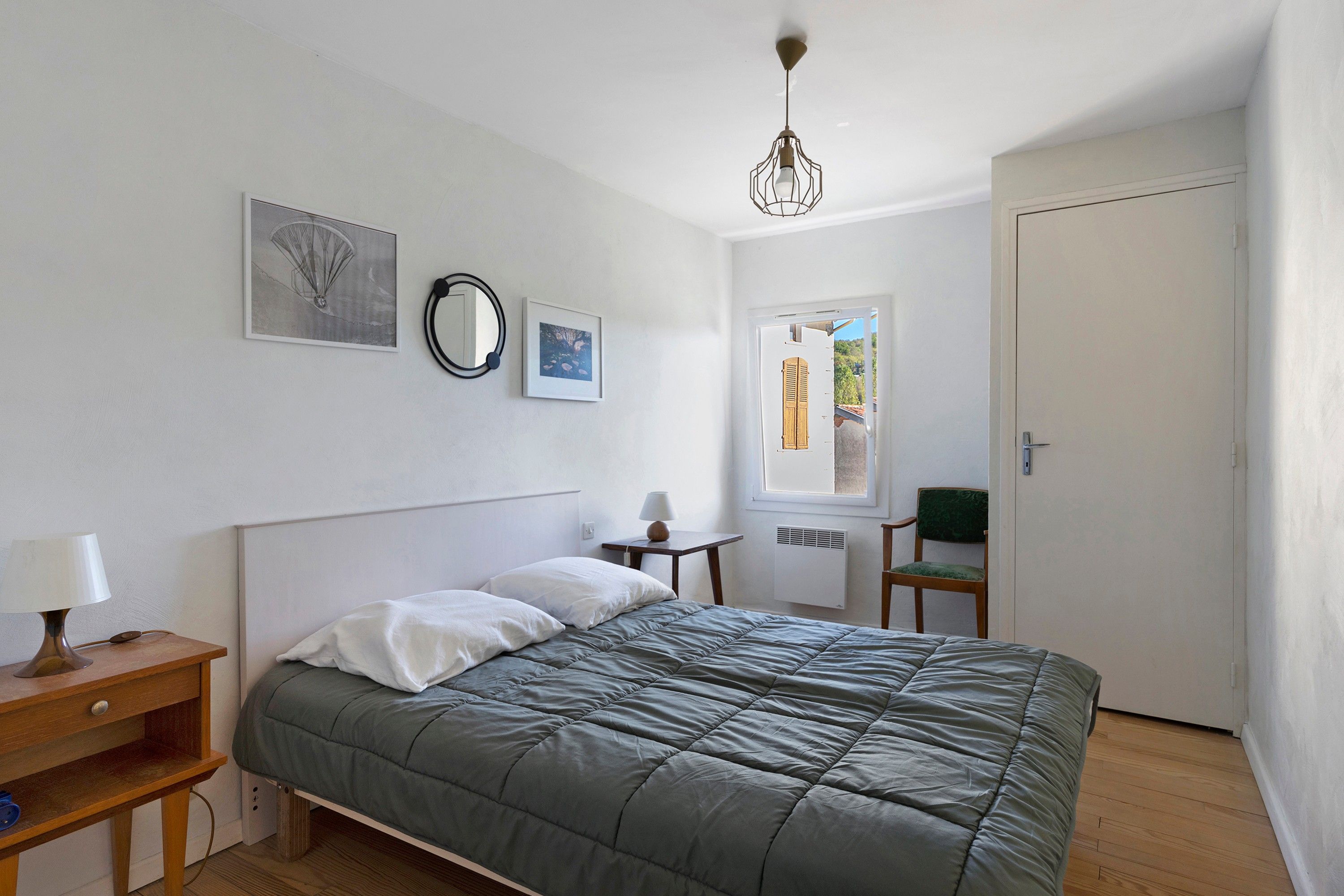 Une chambre à coucher avec un lit, une table de chevet, une lampe et une vue sur l’extérieur.