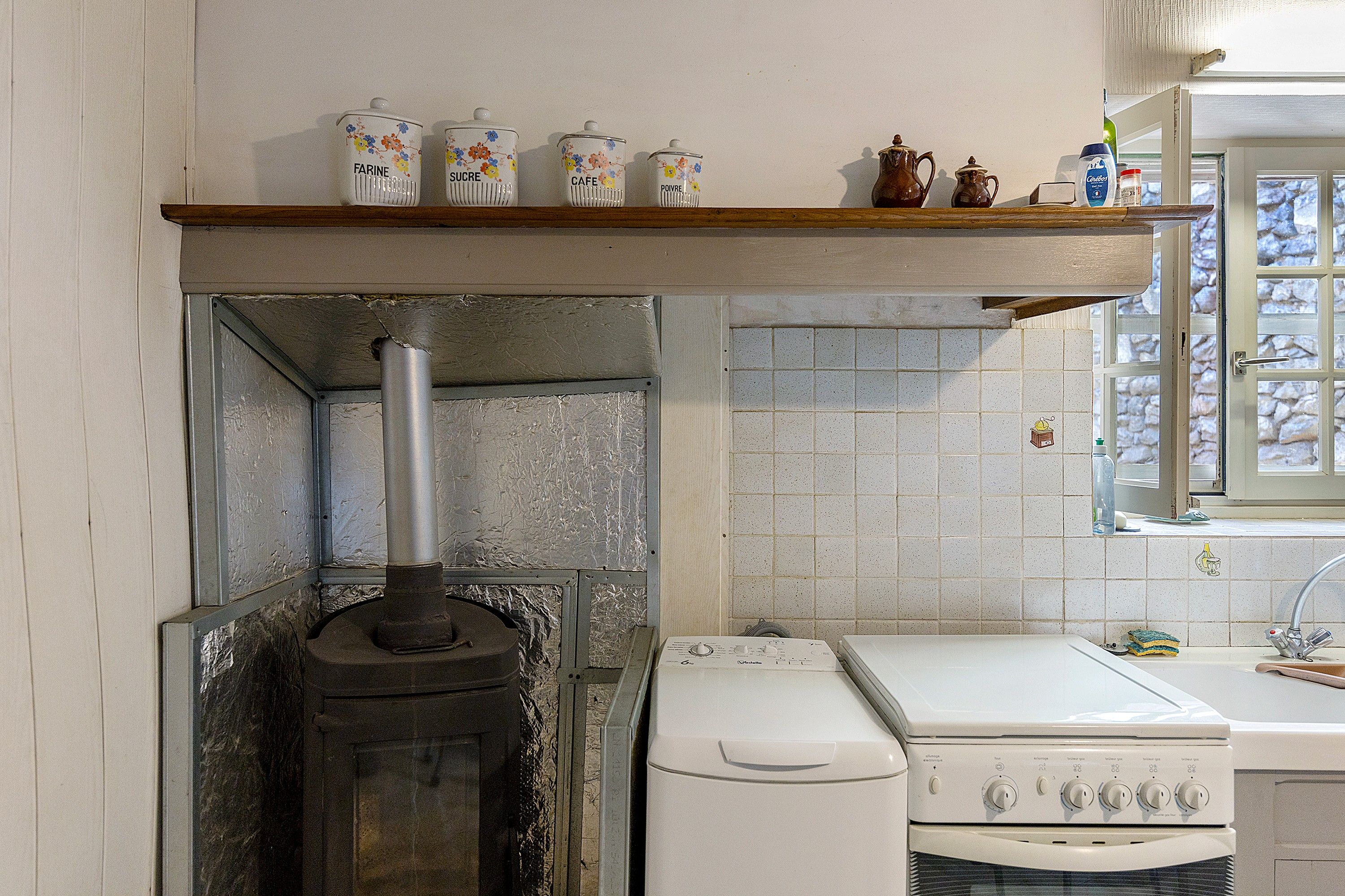 Une cuisine équipée d’un poêle à bois, d’un lave-linge et d’une étagère contenant des ustensiles de cuisine.
