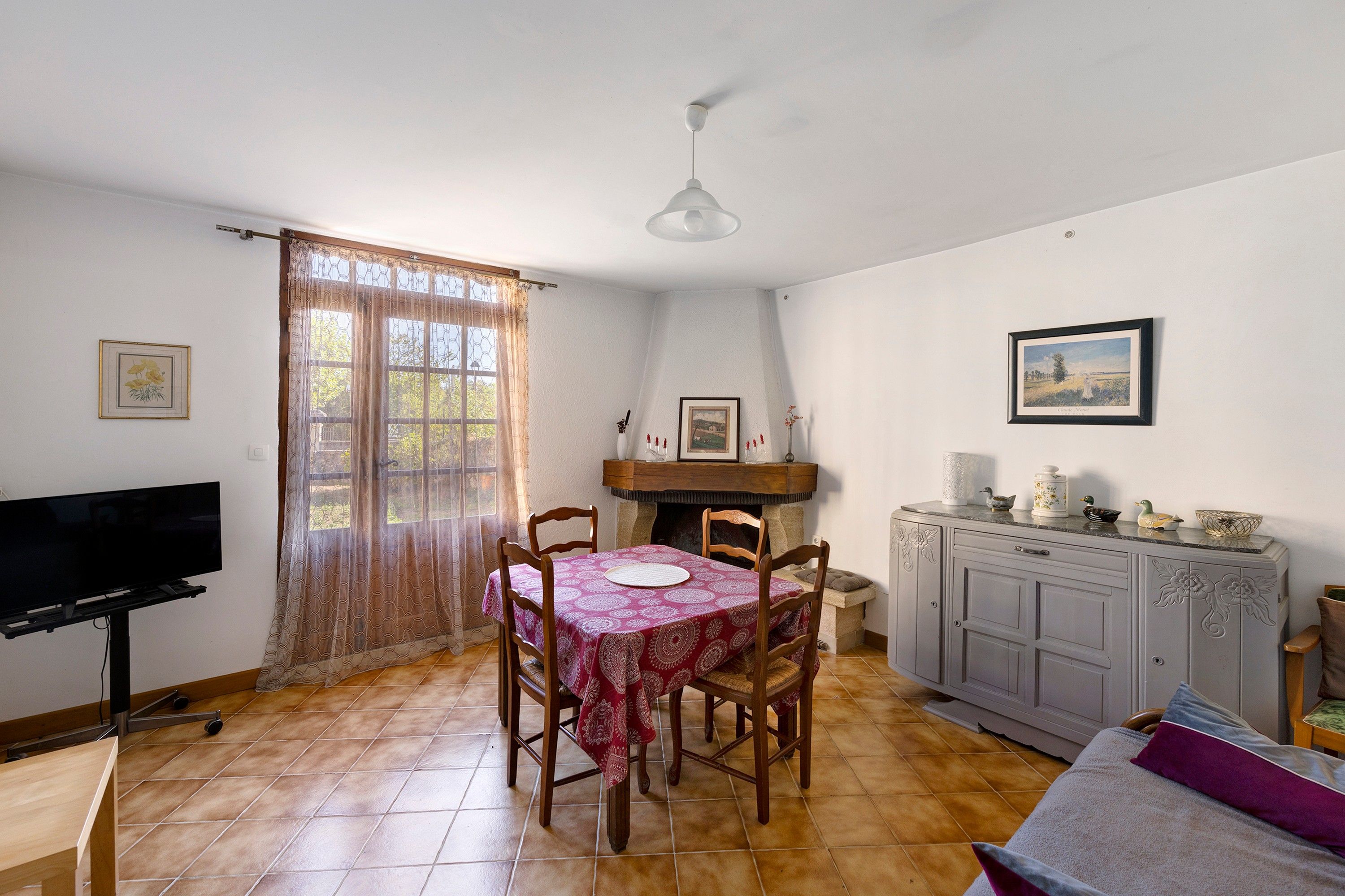 A dining area with a table and chairs, a television, and a cabinet with decorative items.