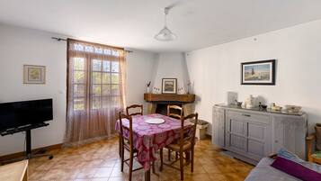 A dining area with a table and chairs, a television, and a cabinet with decorative items.