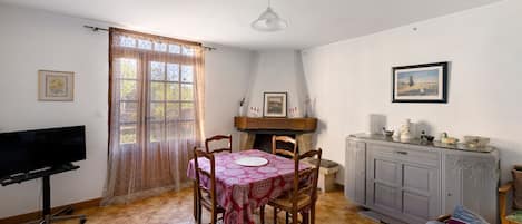 A dining area with a table and chairs, a television, and a cabinet with decorative items.