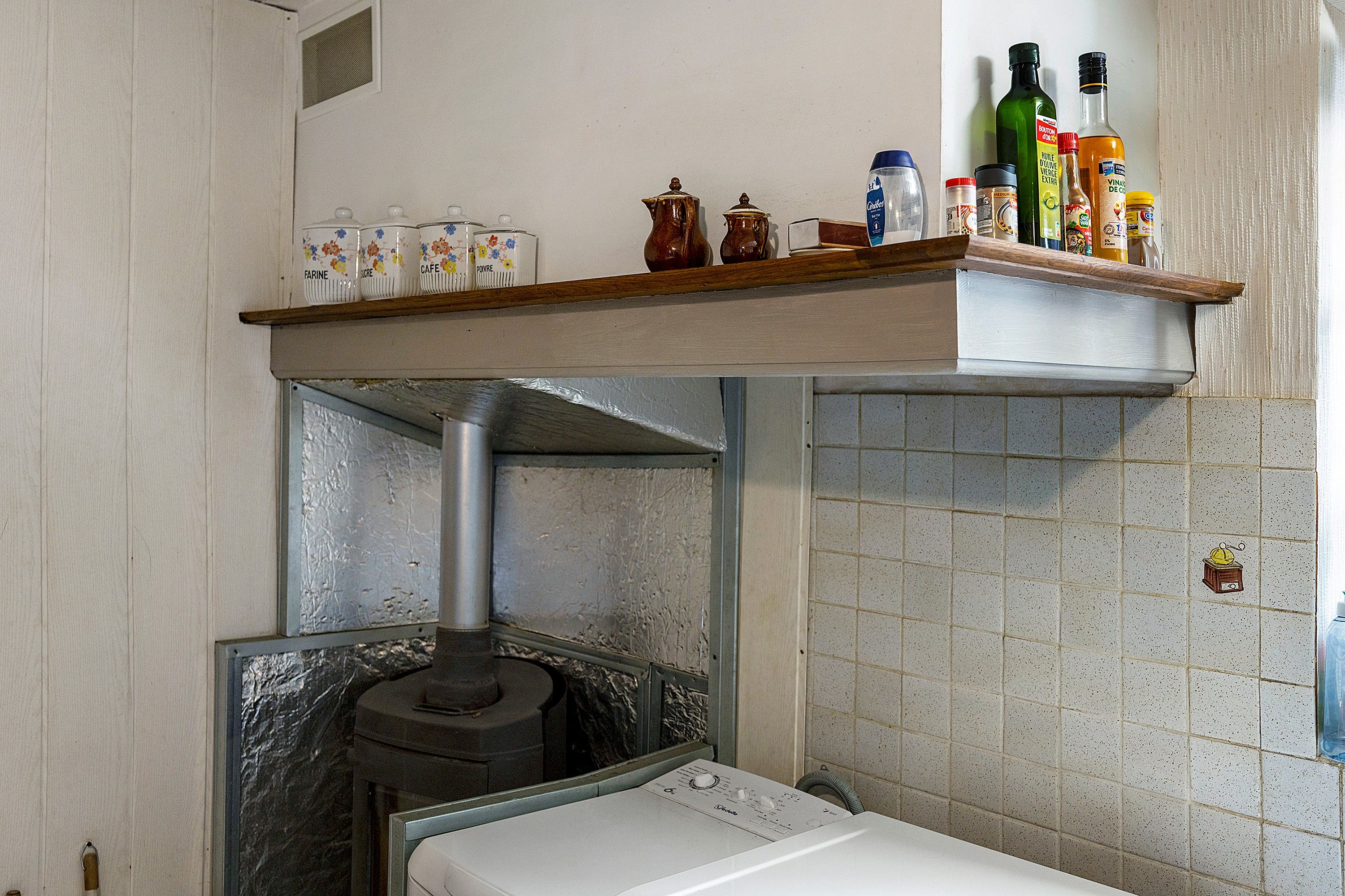 Una cocina con horno empotrado, un estante con diversos utensilios y un salpicadero de azulejos.