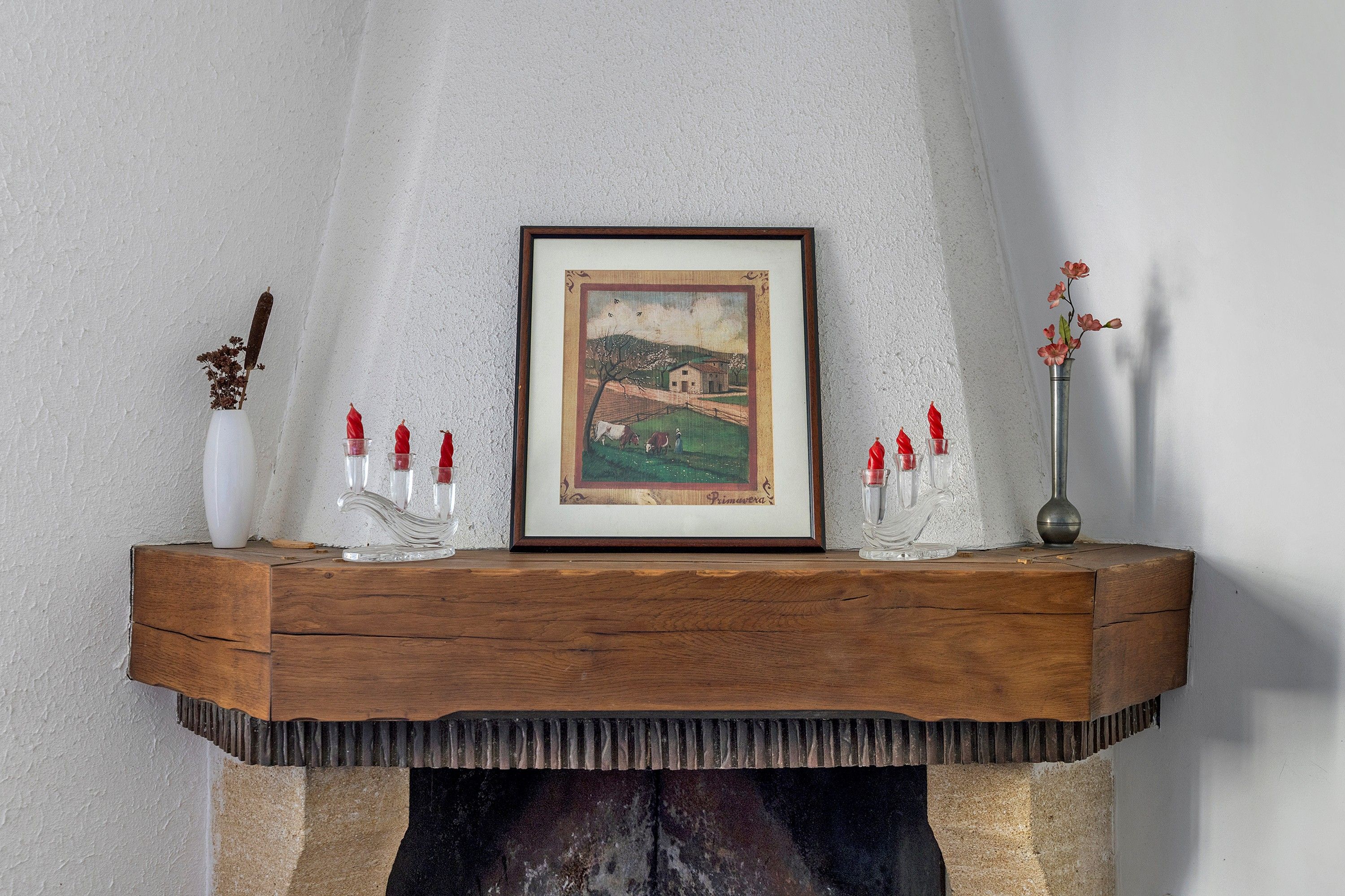 Une cheminée surmontée d’un tableau encadré, de bougies et d’un vase rempli de fleurs.