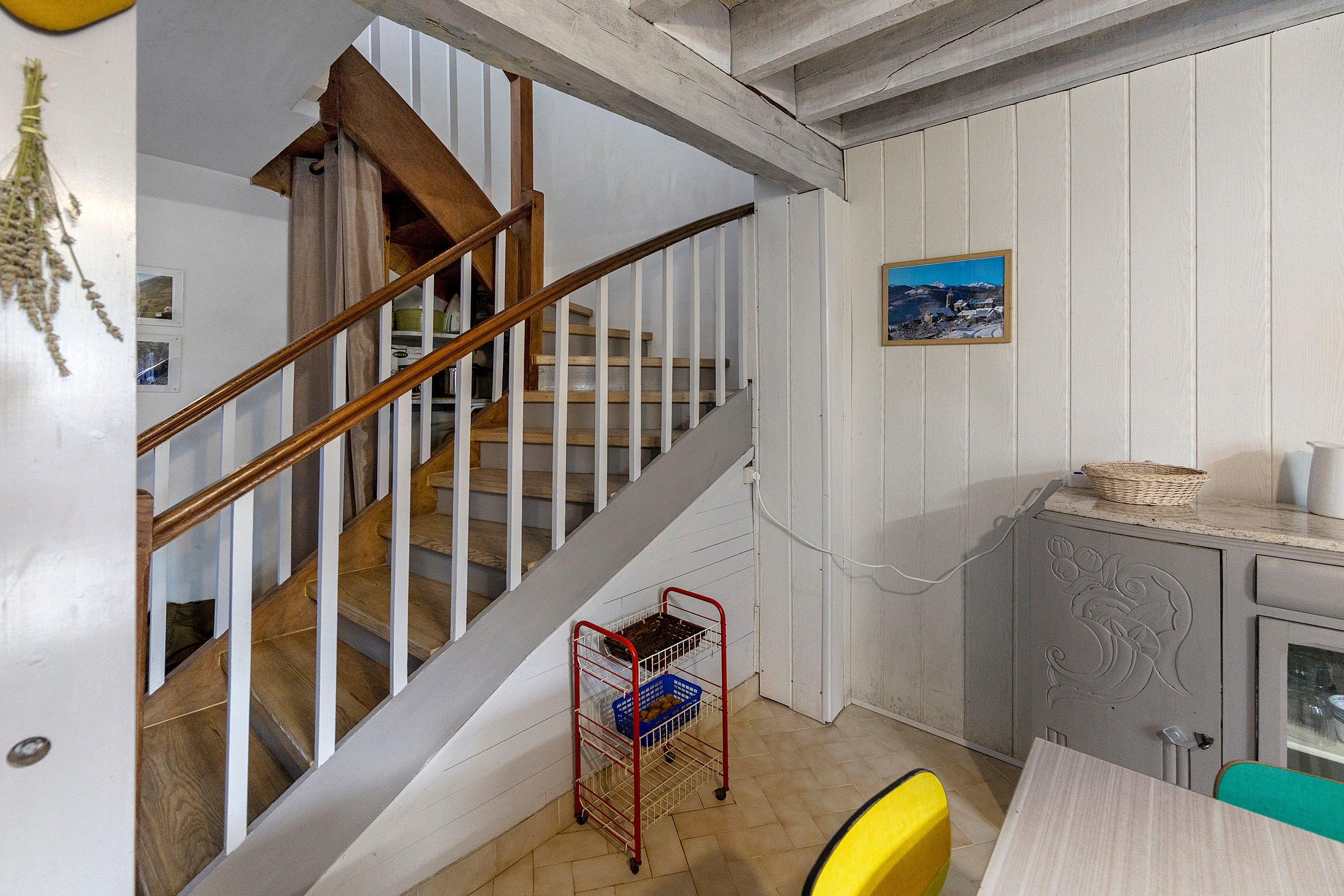 Un escalier avec des rampes en bois et un chariot en métal muni de paniers.