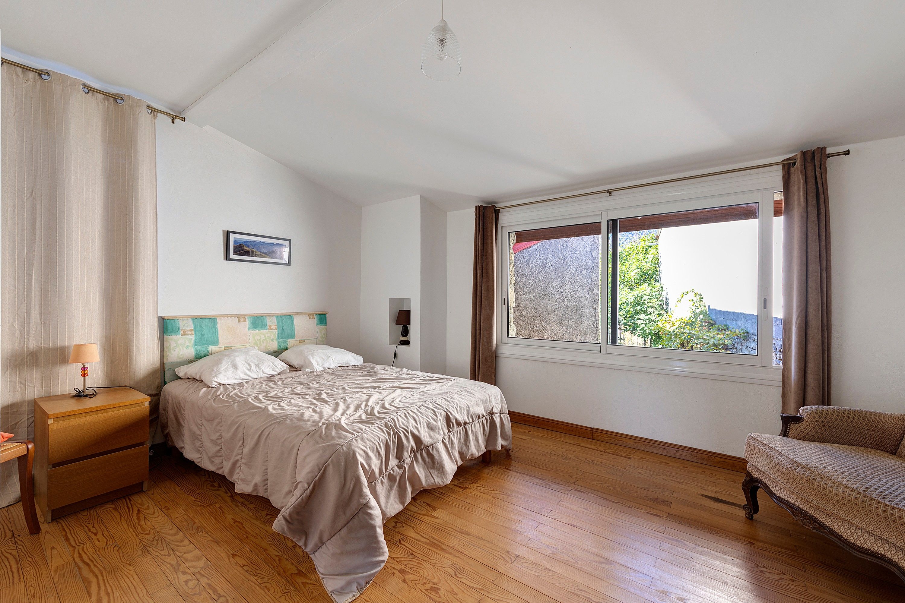 A bedroom with a bed, bedside table, lamp, and a window with curtains.