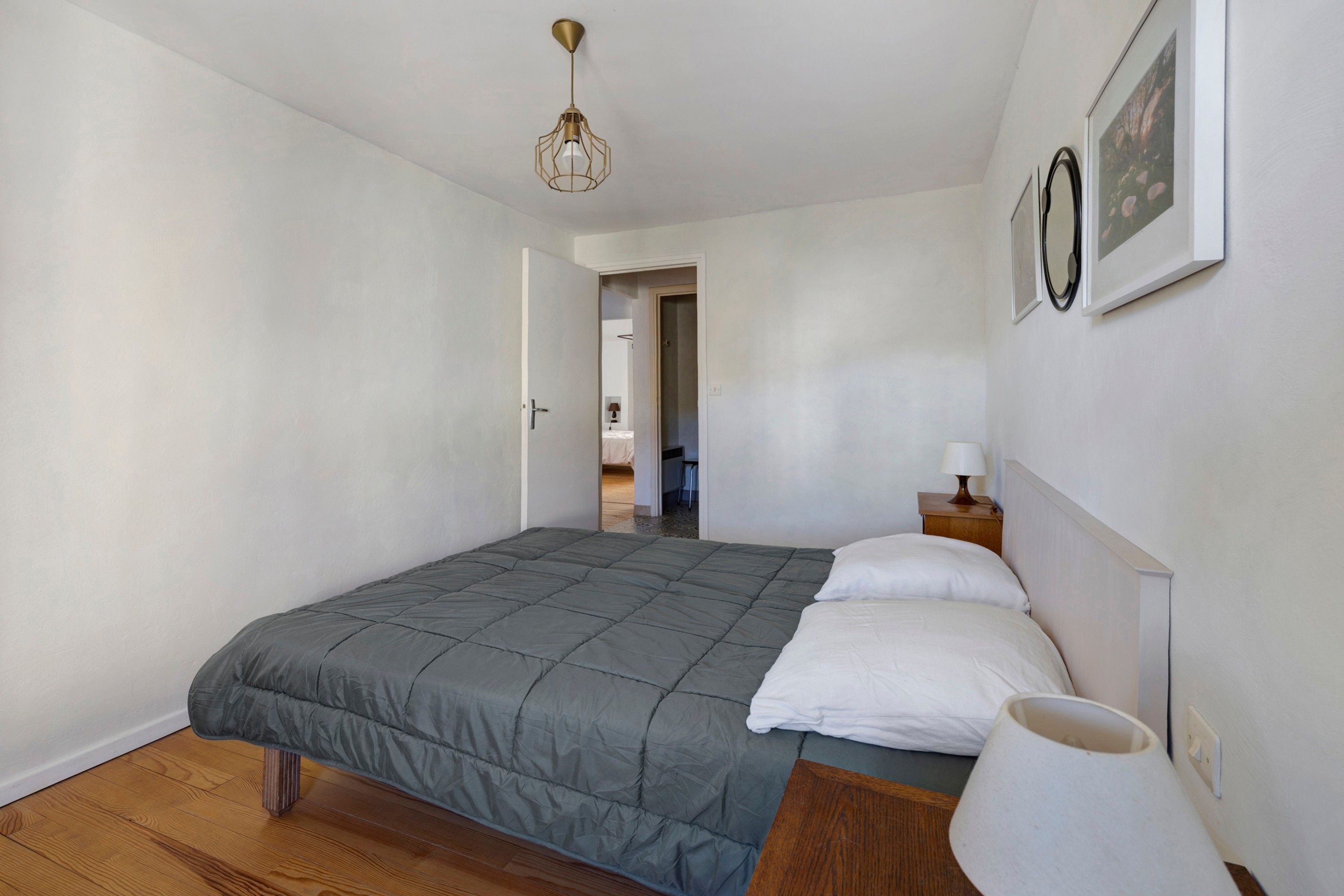Een slaapkamer met een bed, een nachtkastje met lamp, een deur naar een andere kamer en een plafondlamp.
