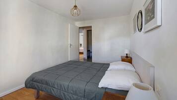 Een slaapkamer met een bed, een nachtkastje met lamp, een deur naar een andere kamer en een plafondlamp.