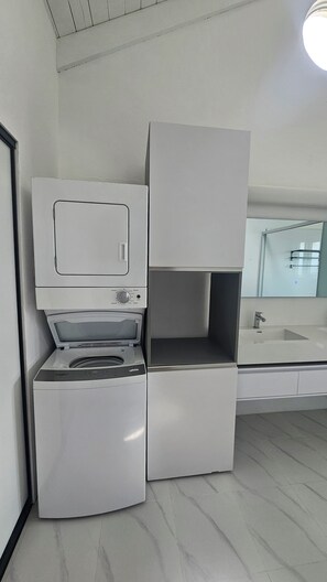 Un baño moderno y funcional con lavadora y secadora integradas, un espejo grande y un lavamanos.