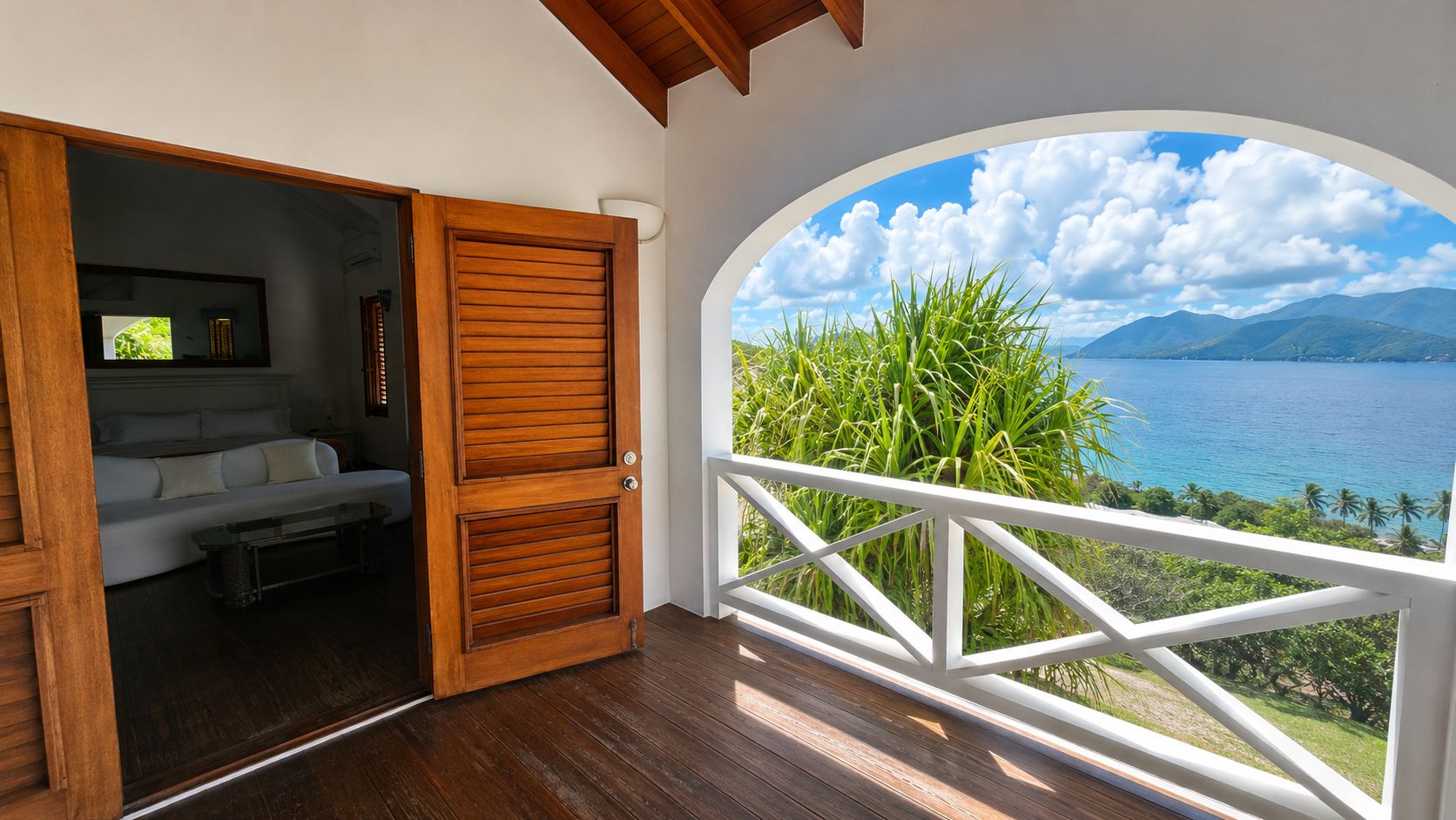 Ein Balkon mit Blick auf einen See und Berge, eine Holztür, die zu einem Raum mit einer Couch und einem Fernseher führt.