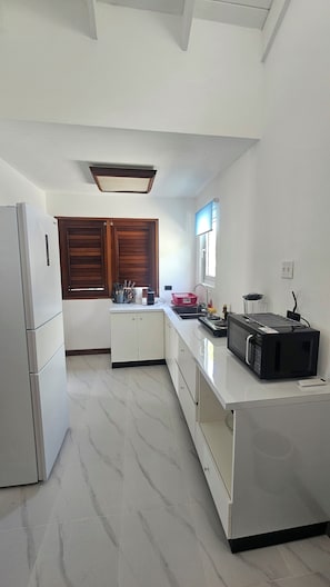 A kitchen with a refrigerator, stove, microwave, and a window with blinds.