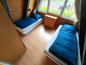 Een kamer met twee bedden, een houten dressoir en een raam met uitzicht op groen.
